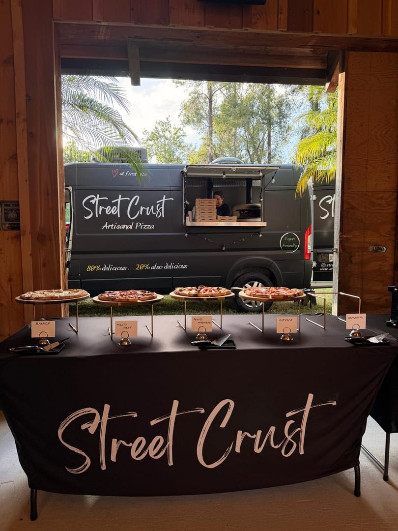 Street Crust artisanal pizza food truck with a variety of pizzas displayed on a branded table.