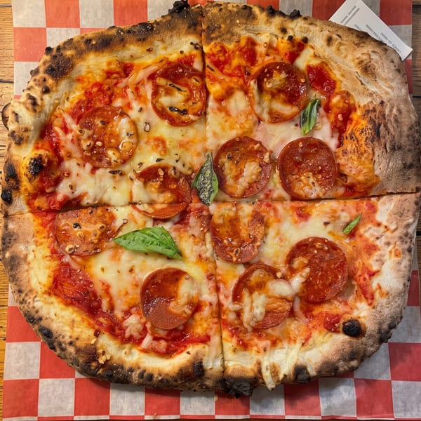 A pepperoni pizza, cut into four slices, on red and white checkered paper.