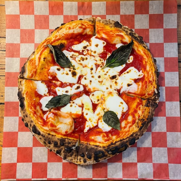 A sliced Margherita pizza with fresh mozzarella, tomato sauce, and basil on checkered paper.