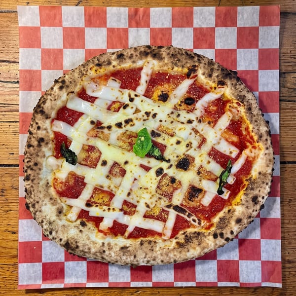 Neapolitan pizza with tomato sauce, mozzarella strips, and basil on a checkered paper.