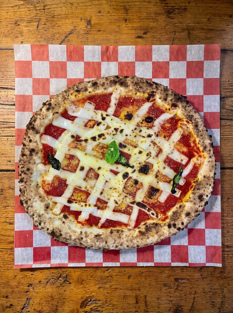 Neapolitan pizza with red sauce, white cheese strips, and basil on checkered paper.