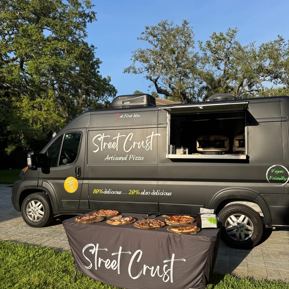 A Street Crust artisanal pizza food truck with a table displaying several pizzas on wooden boards.