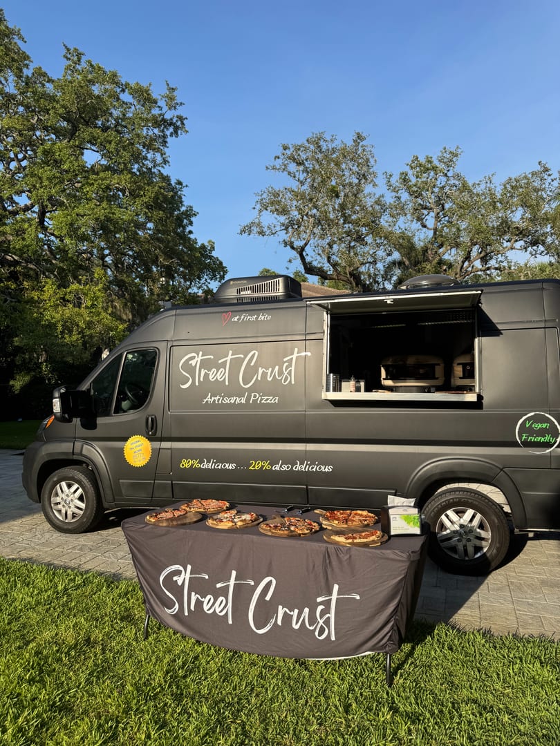 Street Crust Artisanal Pizza food truck with a table displaying various pizzas outdoors.