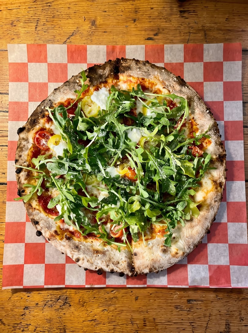 Neapolitan pizza with fresh arugula, burrata, and red sauce on checkered paper.