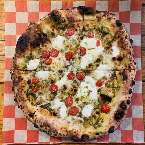 A sliced pesto pizza with fresh mozzarella and cherry tomatoes on checkered paper.